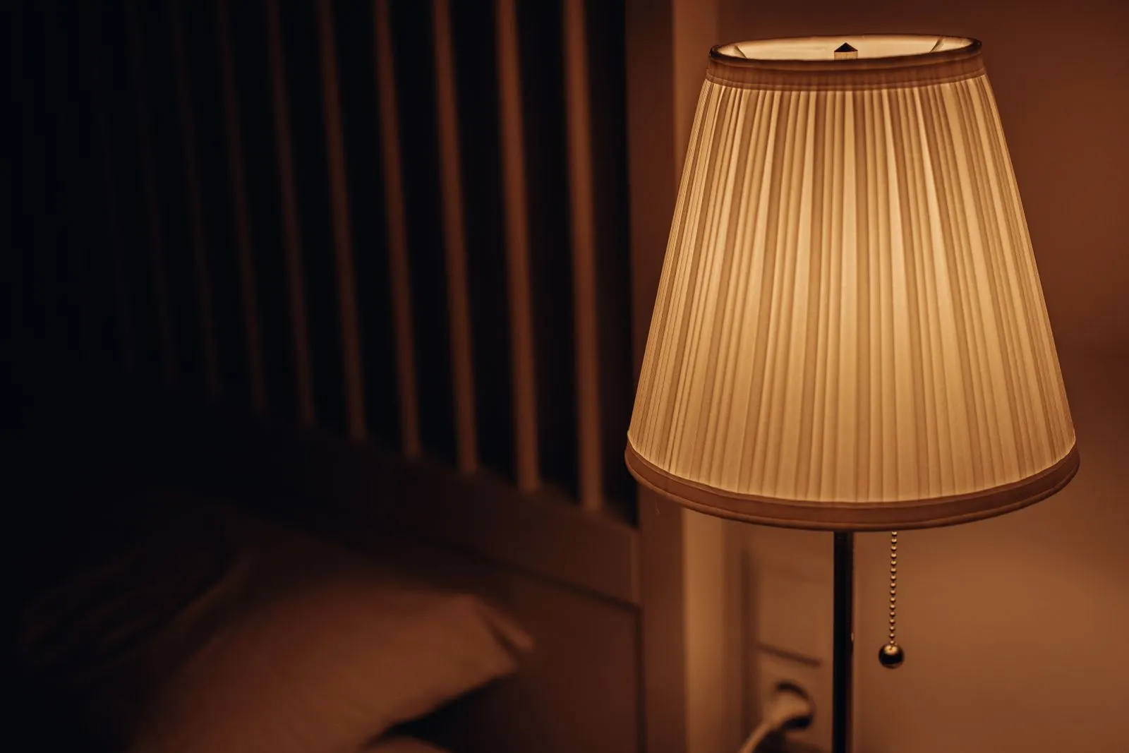 Recámara con luz cálida de lámpara de buró junto a una cama tendida, lista para dormir.